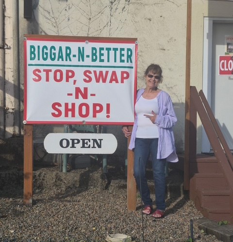 Rexanna Biggar standing beside the Biggar-N-Better Stop, Swap-N-Shop sign in front of the Toledo shop.